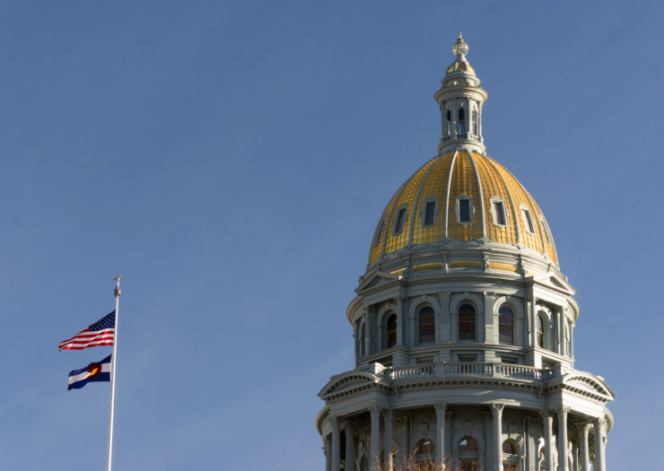 [Photo: The dome of the Denver Capital building with flags flying to the left of it.]