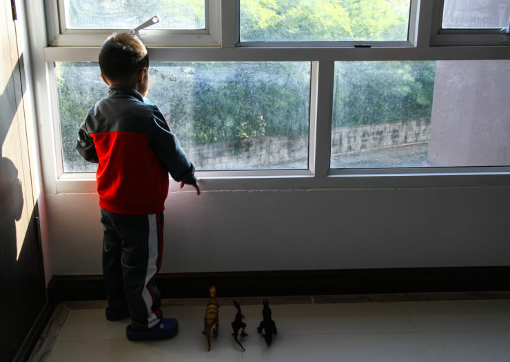 [Photo: A child looks out the window, his back to the viewer]
