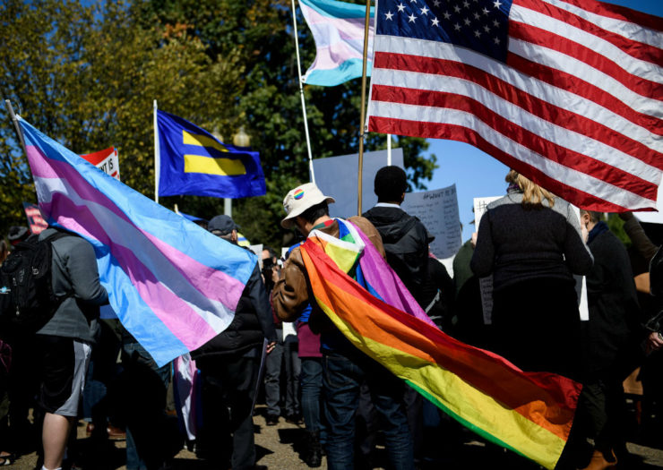 [Photo: Flags being held in the air, including a U.S. flag and a rainbow flag.]