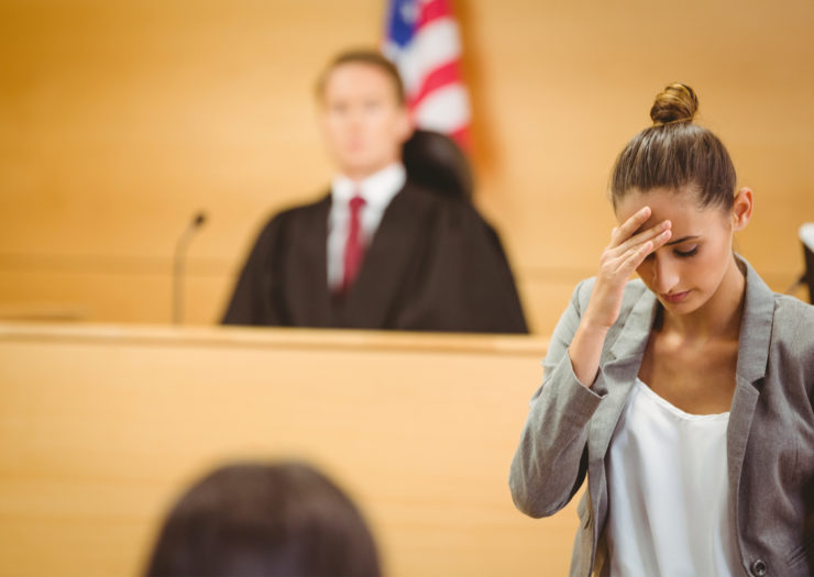 [Photo: A judge looks on as a woman walks away from the bench, hand on her head.]