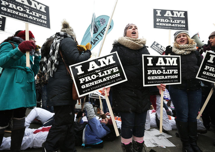 [Photo: Anti-choice activists hold signs at a rally.]