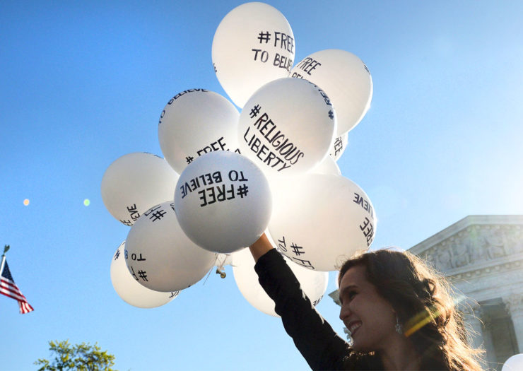 [Photo: Young woman standing in front of a court building with the American flag waving in the background, as she holds numerous white balloons with writing that says 