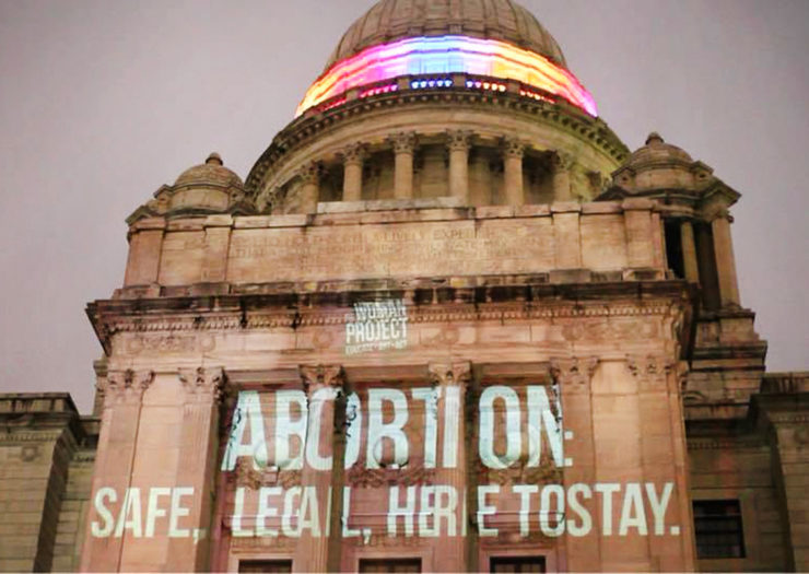 [Photo: Rhode Island State Capitol is pictured with text projected onto it. The text reads 'ABORTION: SAFE, LEGAL, HERE TO STAY.']