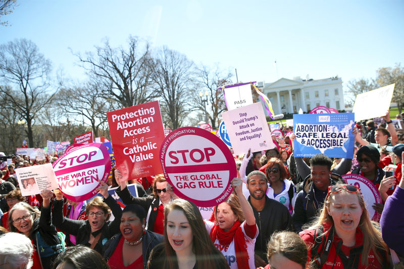 [Photo: Various people ranging in age, size, skin tone and ability gather in front of the White House protesting against Trump's Global Gag Rule.]