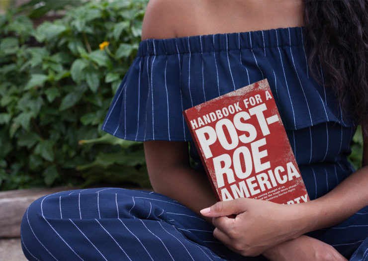[Photo: Young black woman sitting down, holding book entitled 'Handbook for a Post-Roe America.']