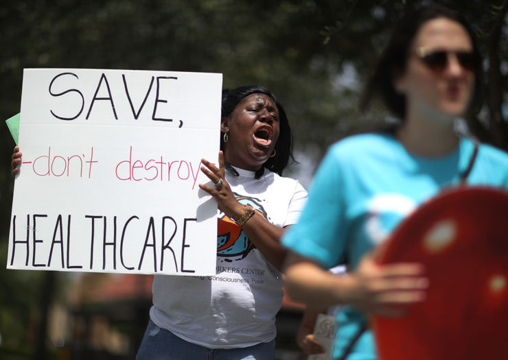 [Photo: Black woman holding sign that says 'SAVE, don't destroy HEALTHCARE' during a rally.]