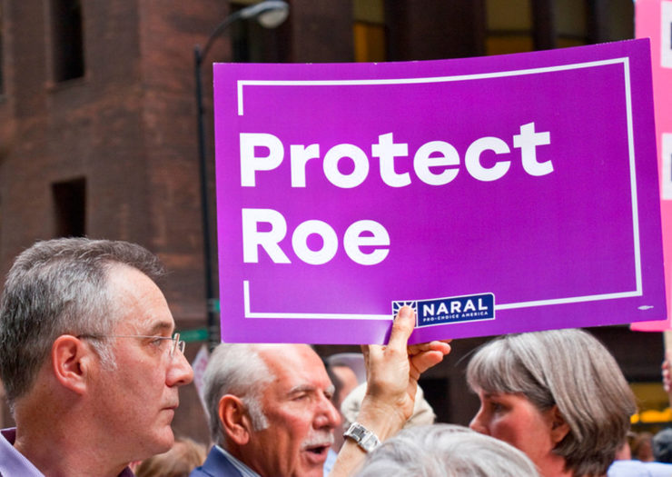 [Photo: A protestor holds a sign that reads 'Protect Roe' during a rally.]