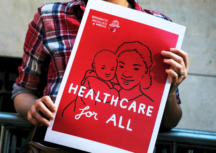 [Photo: A young protestor holds a sign depicting a mother and child which reads 'Healthcare for All.]