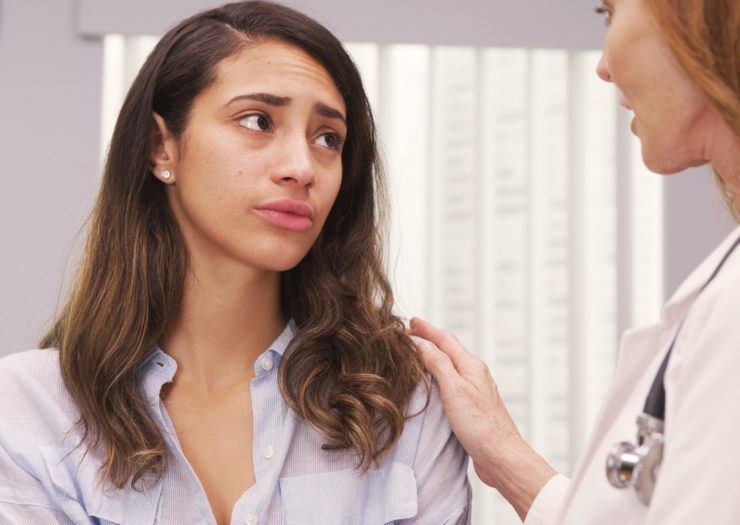 [Photo: A woman of color looks sad and worried as she listens to her doctor.]
