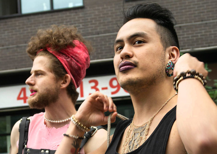 [Photo: Two genderqueer individuals pose for a picture during a parade.]
