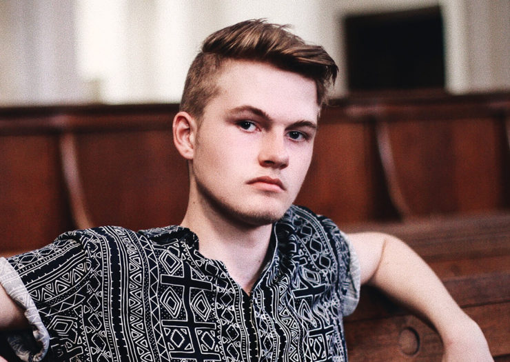 [Photo: Young, white man sits in a church and looks at the camera with an annoyed disposition.]
