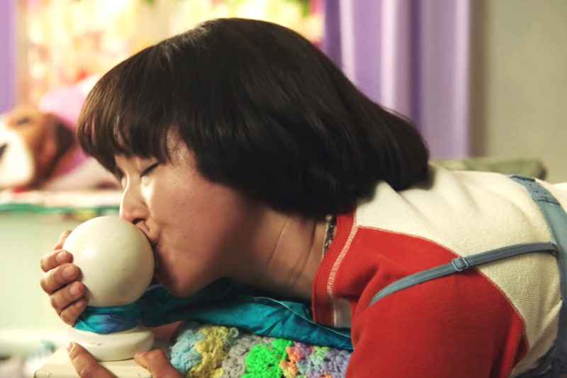 [Photo: Pen15 character Maya practices kissing on a bed post.]