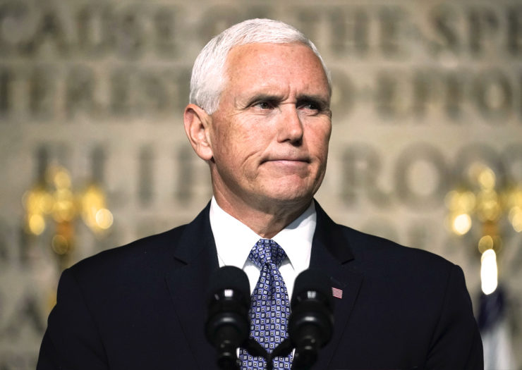 [Photo: Vice President Pence stands behind a podium and reluctantly forces a half-smile as he speaks to the audience.]