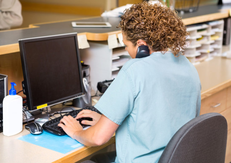 [Photo: A clinic receptionist is talking on the phone and using her computer.]