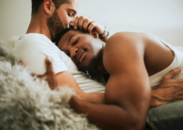 [Photo: Two queer men cuddle on a couch.]