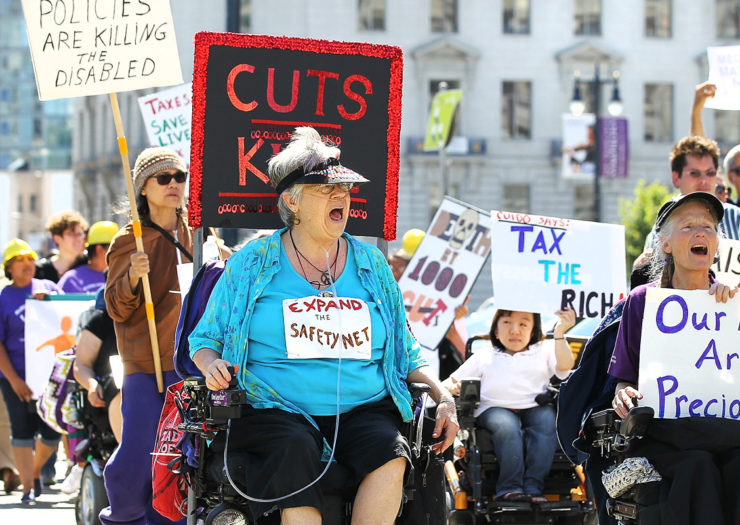 [Photo: Various disabled people of different abilities, ages, skin tones and gender carry signs as they protest cuts to Medicare.