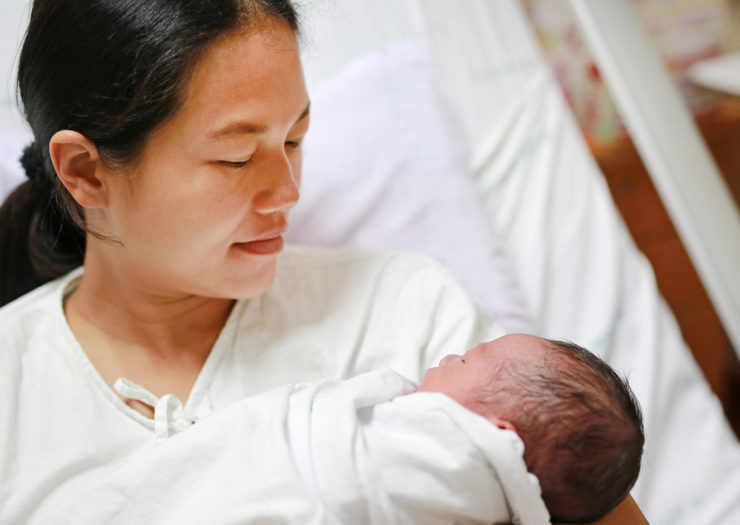 [Photo: Asian mother carrying her newborn.]