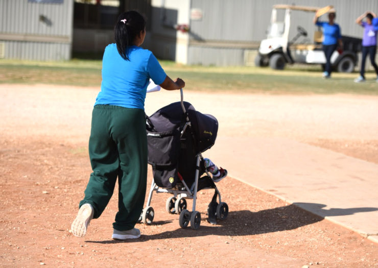 [Photo: A migrant mother in detention pushes her child in a stroller.]