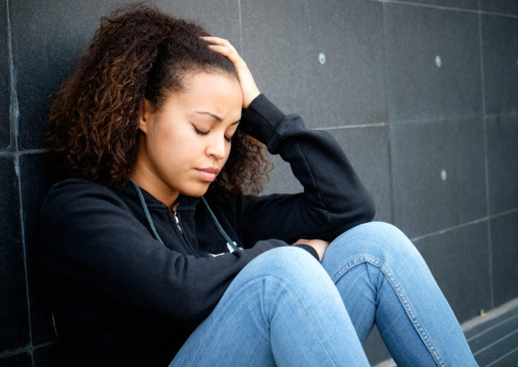 [Photo: A sad and stressed young Black teen sits outside a building.]