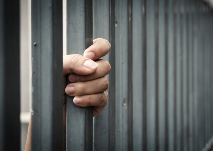 [Photo: Woman of color's hand holding on to cell bars.]