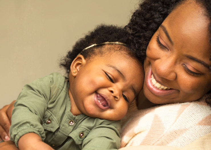 [Photo: A Black mother smiles as she tenderly holds her joyful baby.]