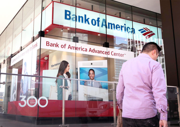 [Photo: A person walks in front of a Bank of America branch.]