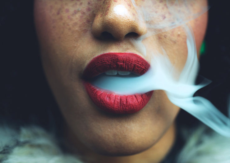 [Photo: A close-up of a young, Black woman's lips as she exhales smoke.]