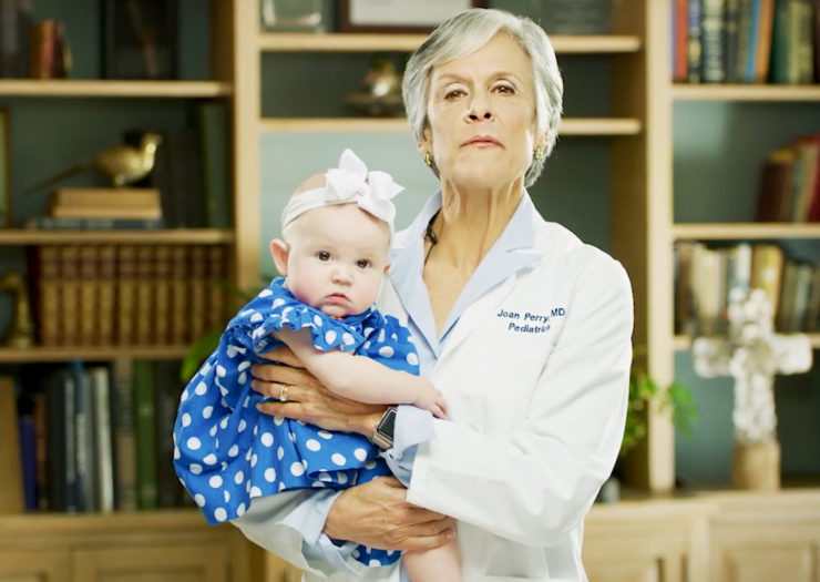 [Photo: Dr. Joan Perry looking resolute while she holds a baby.]