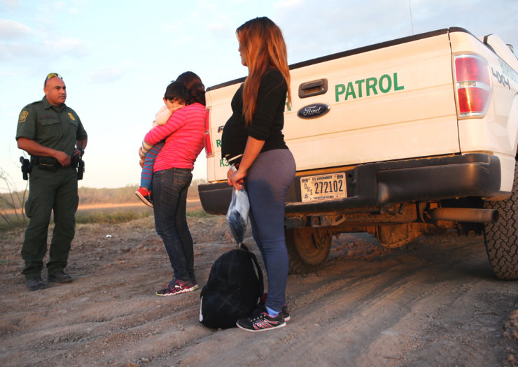 [Photo: An pregnant migrant stands next to a United States Border Patrol truck.]