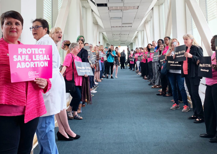 [Photo: A gathering of pro-choice supporters hold up signs that read 'Stop SB1774' and 'Protect Safe, Legal Abortion.']