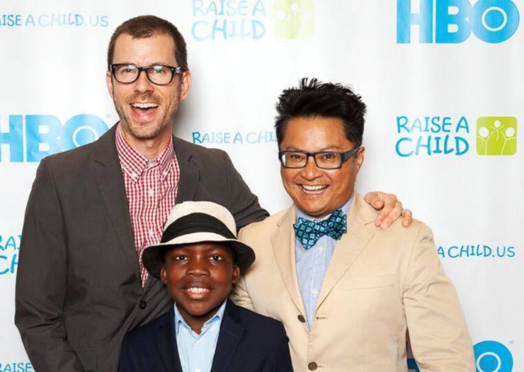 [Photo: Jamie Hebert [L), Alec Mapa and their son, Zion, smile and pose for a picture at an event.]