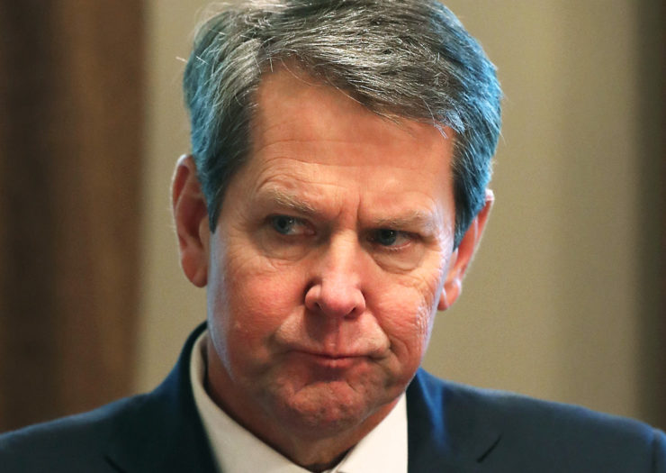 [Photo: Governor Brian Kemp listens on during an event.]