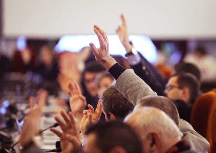 [Photo: Male legislators vote by raising their hands.]