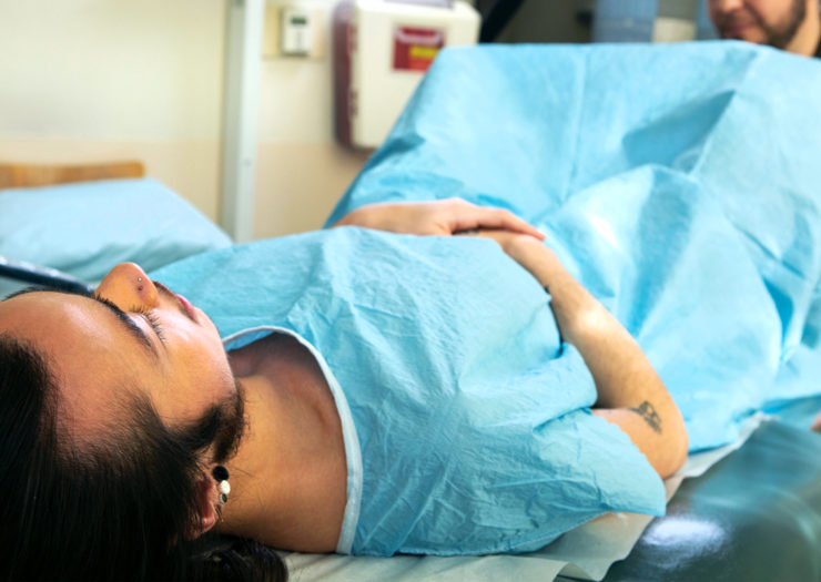 [Photo: A non-binary person wears a gown while they lie down for a pelvic examination.]