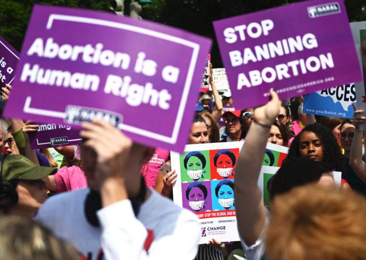 [Photo: A crowd of pro-choice advocates holding signs gather to protest abortion bans.]