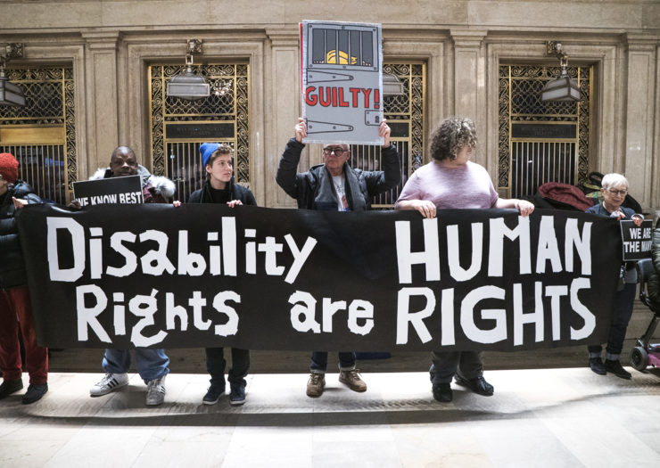 [Photo: Disability rights demonstrators hold a banner that reads 'Disability Rights are Human Rights.']