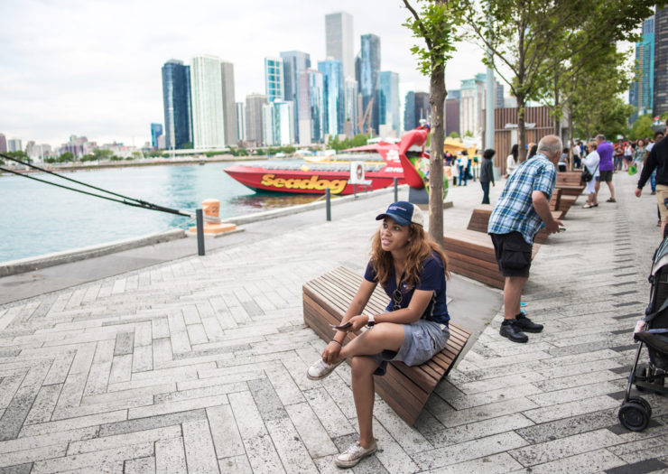 [Photo: A young, Black woman sits by the Navy Pier in Chicago.]