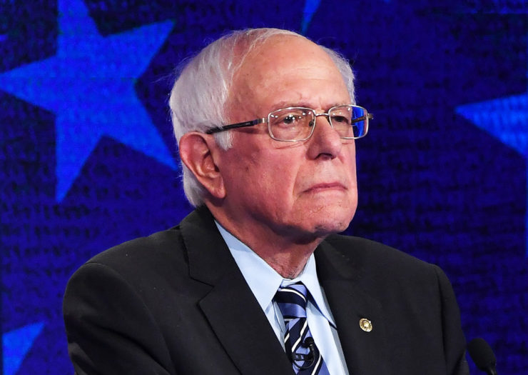 [Photo: Senator Bernie Sanders looks on during a debate.]