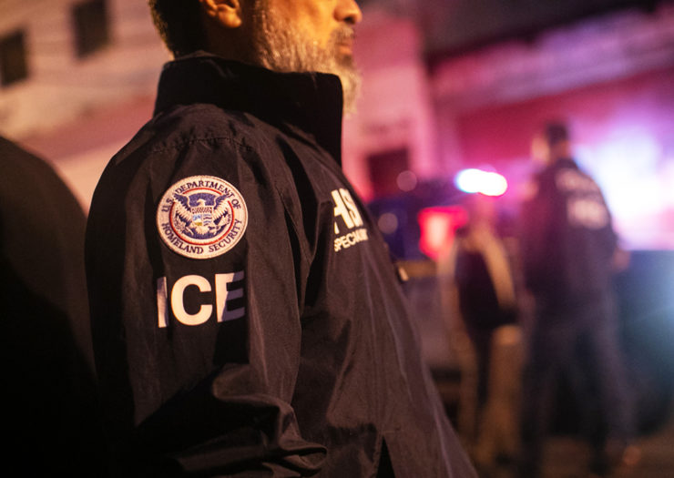 [Photo: An ICE agent looks on during a night investigation.]