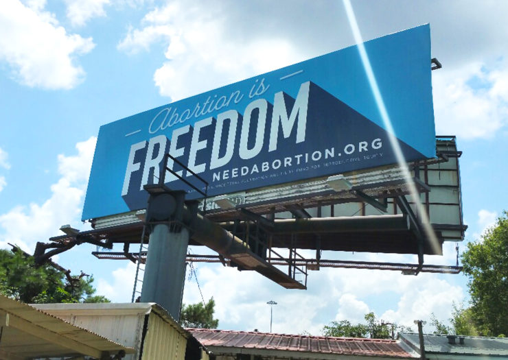 [Photo: A large billboard that reads 'Abortion is Freedom’ rises between buildings.]
