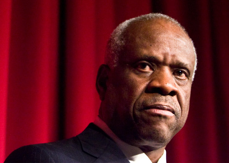 [Photo: U.S. Supreme Court Justice Clarence Thomas listens on during an event.]