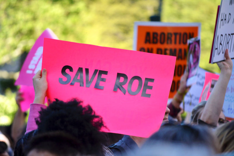 [Photo: A person holds a pink sign that reads 'Save Roe' during a rally to protest in support of abortion rights.]