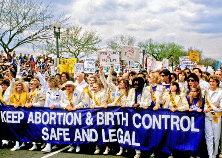 [Photo: A trove of pro-choice supporters hold a large, blue banner that reads 'KEEP ABORTION & BIRTH CONTROL SAFE AND LEGAL' during an event.