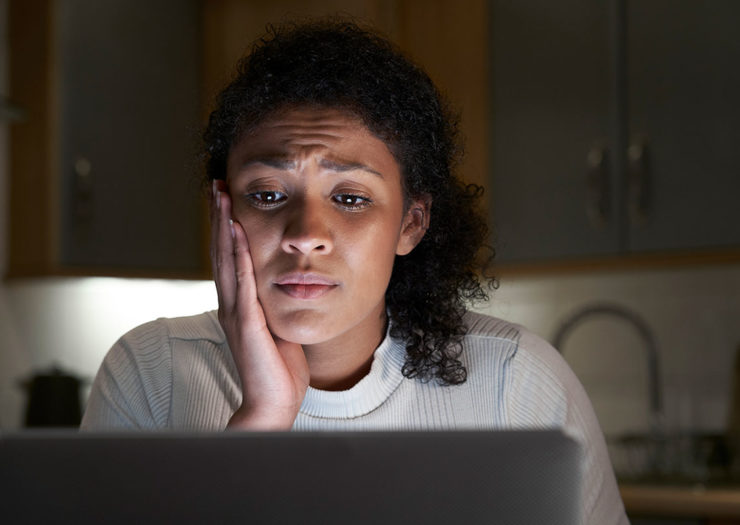 [Photo: A young Black woman with a worried expression looks at her laptop.]