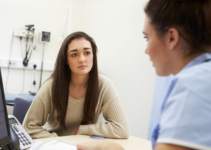 [Photo: A young woman speaks to her doctor.]