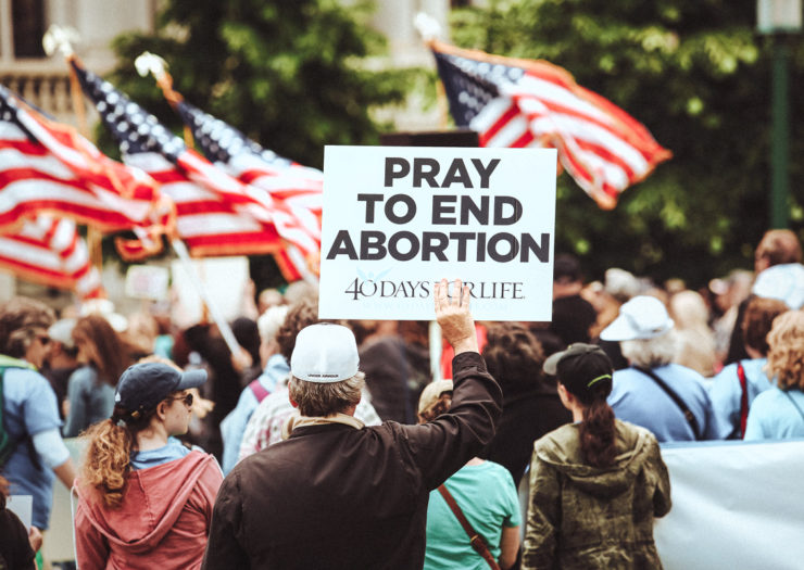 [Photo: Anti-choice supporters hold signs and flags as they rally.]