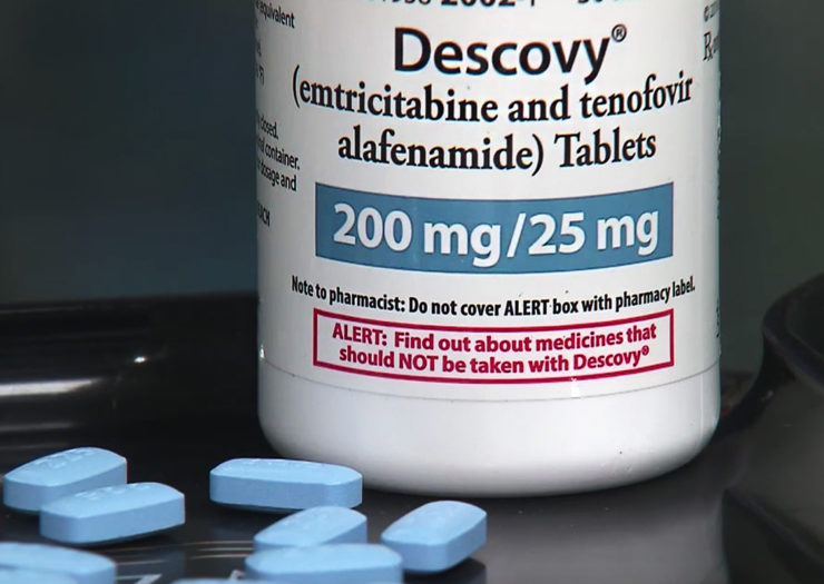 [Photo: A bottle of Descovy sits on a table with blue pills in the foreground.]
