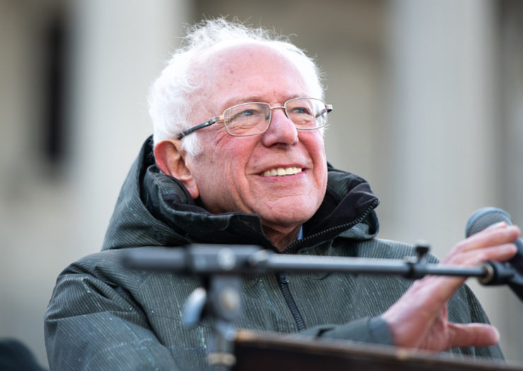 [Photo: Democratic presidential candidate, Sen. Bernie Sanders smiles as he addresses a crowd.]