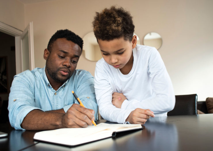[Photo: A Black father and son do homework together.]