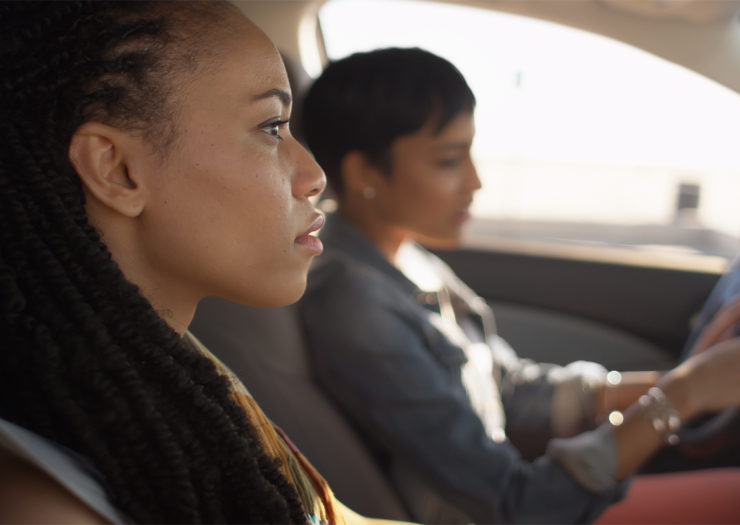 [Photo: Two young, Black women in a car. The woman in the passenger seat looks concerned.]